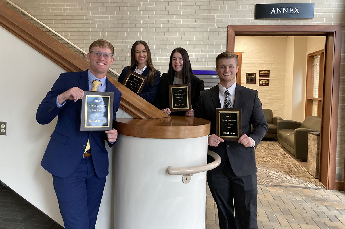 four students in suits posing with award plaques